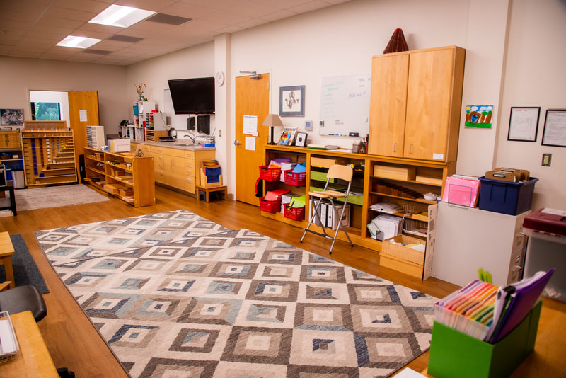 This image features the right wall in the classroom showing a tv screen, more shelves with materials and works, a white board, as well as two doors - one peeking into the library.
