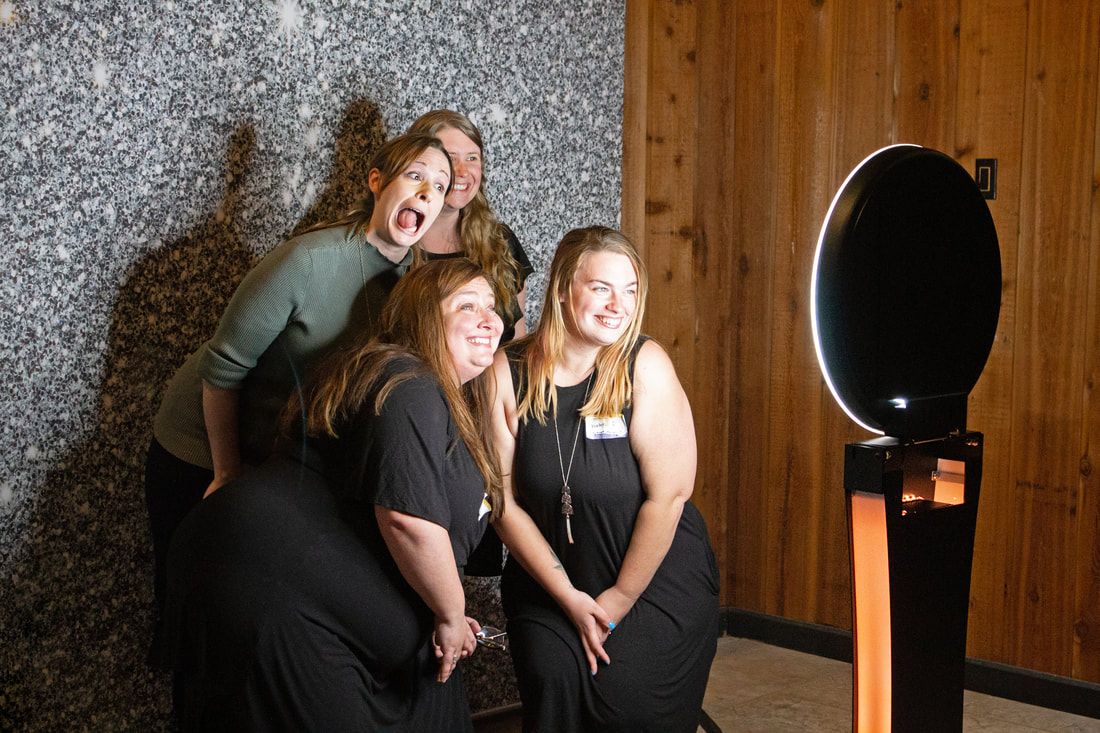 Four staff members making silly faces and smiling at the stand alone Photo Booth with sparkle background.