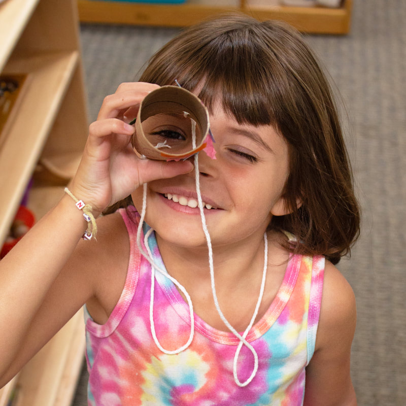 Kindergartener with lots of excitement looking with one eye through a handmade telescope made from a toilet paper roll and yarn.