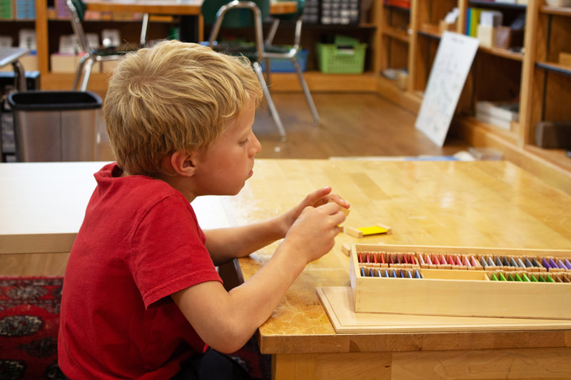 Side of student wearing red shirt is shown with deep concentration as they focus on the subtle hue changes in the tile in their hand. They just begun on yellow.
