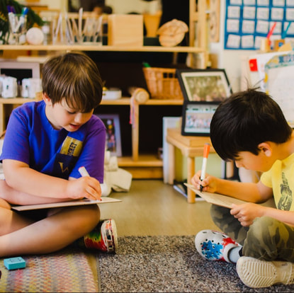 Two children holding a camera attempting to photograph some language works in a Montessori classroom